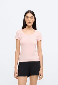 Rózsaszín rövid ujjú póló kerek nyakkivágással. Az anyag sima és könnyű. Fekete rövidnadrággal párosítva, egyszerű kialakítással.