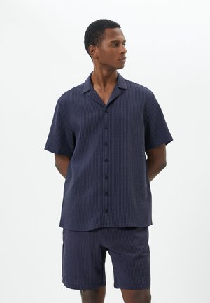 Kurzarmhemd mit Navy-Muster und Knopfverschluss, kombiniert mit passenden Shorts. Weicher Stoff mit einer dezenten gerippten Textur.