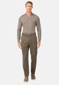 Světle hnědý vlněný polo s dlouhým rukávem a výstřihem do V, zkombinovaný s khaki společenskými kalhotami s záhyby; model má na sobě béžové boty.