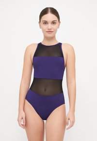 Maillot de bain une pièce violet avec une section médiane en maille transparente et un tissu solide en haut et en bas. Texture lisse avec un col montant et un dos nageur.