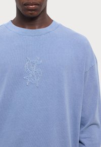 Felpa azzurra con colletto a coste, caratterizzata da un logo di dollaro ricamato e testurizzato sul petto. Tessuto in cotone morbido.