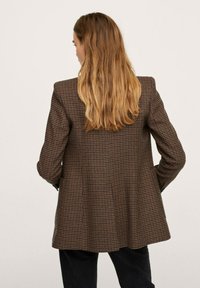 Blazer a cuadros marrón con corte relajado, presenta una textura suave y solapas afiladas, acentos de costura visibles y un diseño clásico.