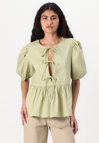 Blusa verde pallido con maniche a sbuffo, dettagli a fiocco al collo e vita arricciata, realizzata in un tessuto leggero.