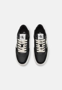 Zapatillas negras con cordones blancos, con un upper de cuero suave, acentos en contraste y un perfil bajo. Logo en la lengüeta.