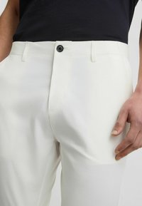 Białe spodnie o gładkiej fakturze, z czarnym zapięciem na guzik, przednimi kieszeniami i prostymi nogawkami. Minimalistyczny styl.