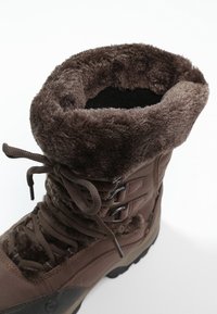 Botas marrones aisladas con un suave forro de piel texturizada en el cuello, con cordones en la parte delantera y suela de goma. Tejido duradero para uso al aire libre.