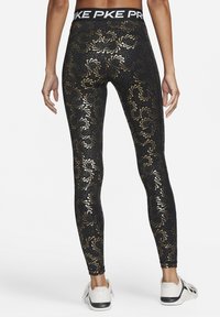 Leggings negros con un patrón floral dorado y acentos de puntos. Presentan una cinturilla ancha negra con el nombre de la marca en blanco.