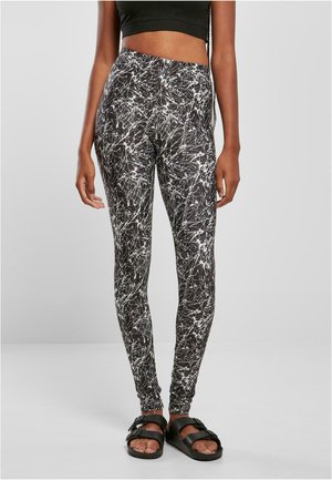 Black leggings with a white abstract splatter pattern, made from a stretchy material. Paired with flat black sandals.
