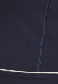 Tumesini sweatshirt kangas, mis on sileda tekstuuriga, kontrastsete valgete soontega õmbluste ääres ja silmapaistvate lamedate õmblustega detailiga.