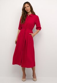 Fuchsia skjortklänning med korta ärmar, knapplist fram, bältesmidja och sidofickor. Slät tyg med en lätt A-linjeformad silhuett.