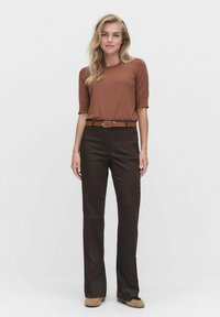 Bruine korte mouw top in combinatie met donkerbruine high-waisted broeken, aangevuld met een brown ceintuur. Rechte pijpuitvoering, gladde stoffen textuur.