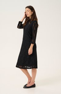 Robe en dentelle noire avec des manches trois-quarts, de forme A, motif floral et ourlet à volants. Associée à des ballerines noires.