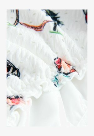 Biela bavlnená tkanina s textúrovaným povrchom, ktorý obsahuje farebnú kvetinovú výšivku v ružovej, červenej a zelenej farbe. Riasené okraje ako detail.