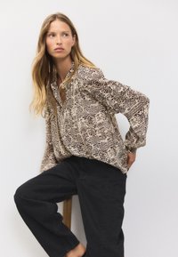 Long-sleeve beige shirt with black geometric patterns, featuring a collar and button front, paired with black trousers in soft fabric.