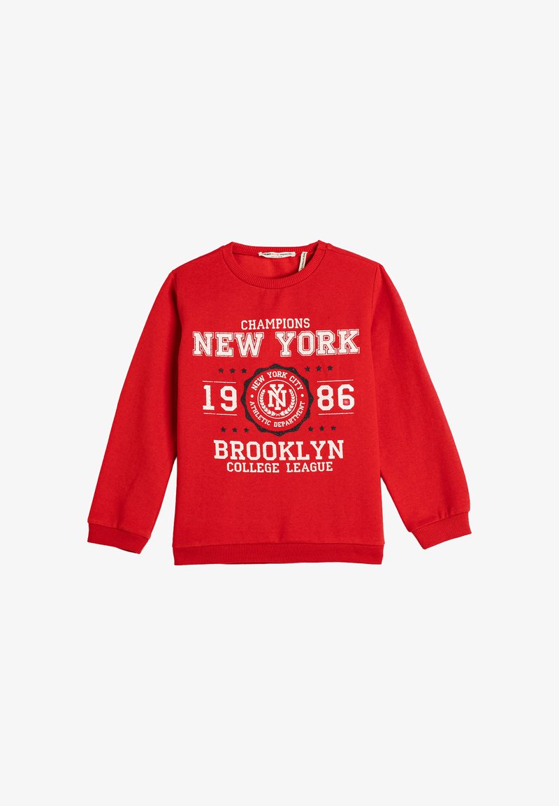 Czerwona bluza z długim rękawem z białym napisem "Champions New York 1986 Brooklyn College League" oraz okrągłym emblematem Nowego Jorku.
