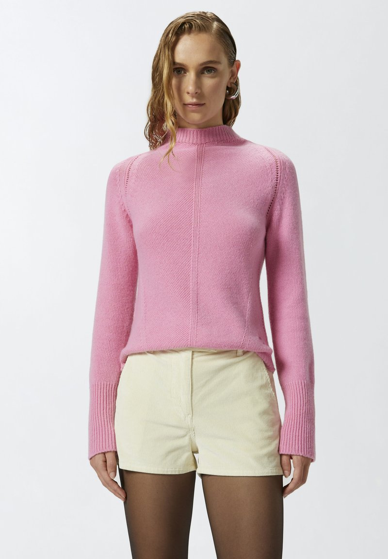 Sweatshirt en tricot rose ajusté avec un col haut, des poignets côtelés et un motif texturé, associé à un short en velours côtelé jaune clair.