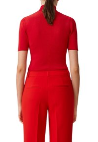 Top rojo de manga corta con cuello alto, acabado de punto texturizado y detalle de costura vertical en la espalda, combinado con pantalones a medida rojos a juego.