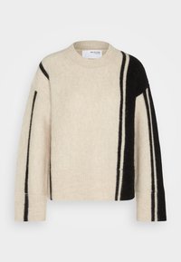 Beige svetr s volným střihem, který má černé pruhy na jedné straně a žebrované manžety. Vyrobeno z měkké, strukturované látky.
