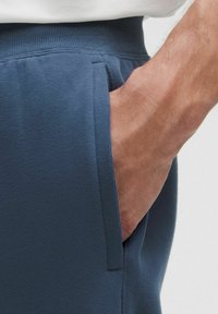 Hand in een zijzak van blauwe gezepte stof joggingbroek met een elastische tailleband.