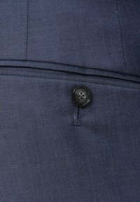 Tessuto blu navy caratterizzato da una trama diagonale, con un piccolo bottone nero e una sottile accentuazione di cuciture. Un design classico su misura.