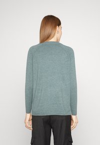 Cardigan in un teal chiaro con maniche lunghe e scollo rotondo, realizzato in un materiale morbido e testurizzato, caratterizzato da una vestibilità rilassata e senza chiusure visibili.