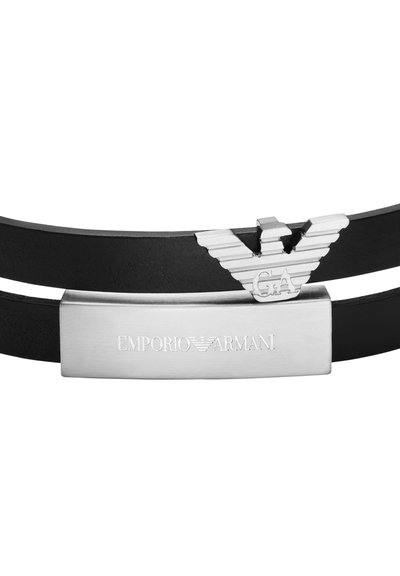 Bracelet en cuir noir présentant un emblème argenté avec des ailes et la gravure "EMPORIO ARMANI" sur une plaque métallique rectangulaire.