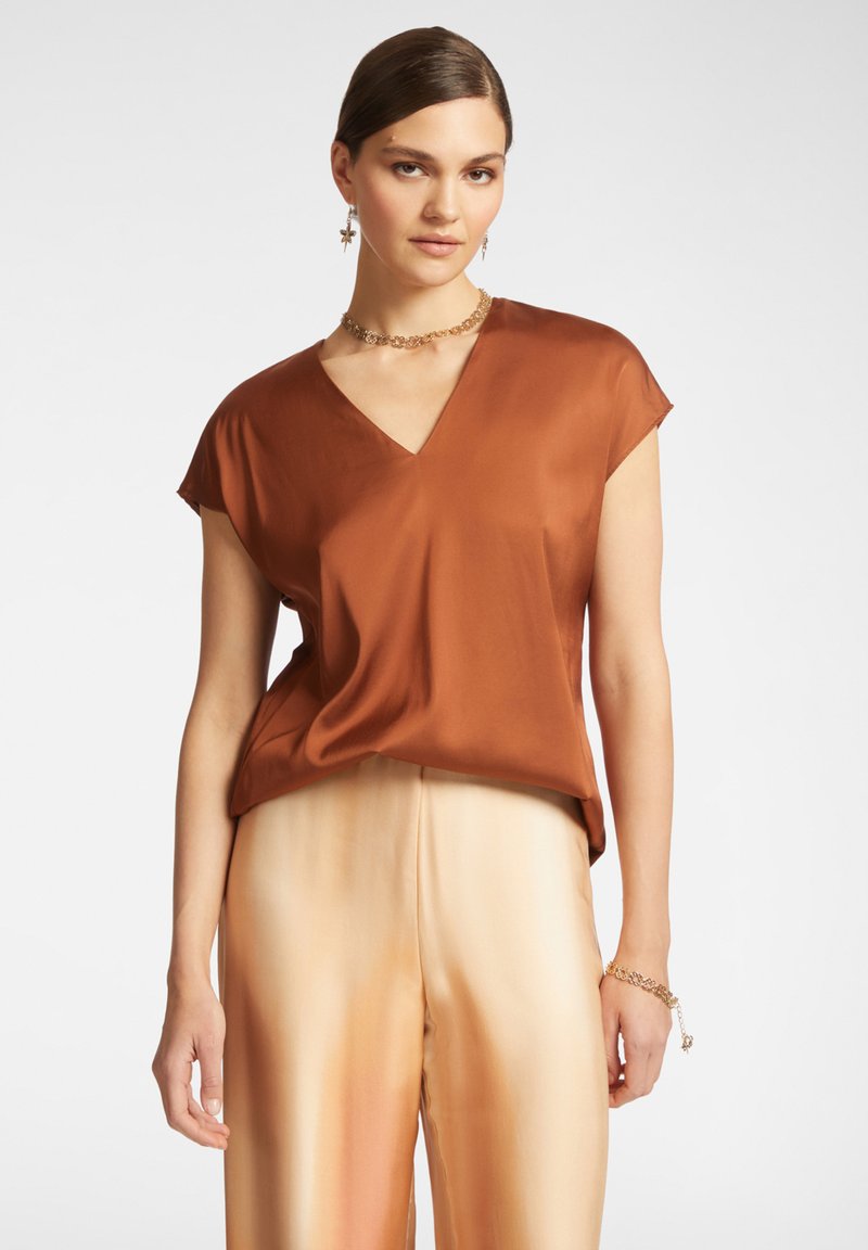 Blusa di raso marrone con scollo a V, maniche corte e vestibilità ampia, abbinata a pantaloni di raso beige ombré chiaro.