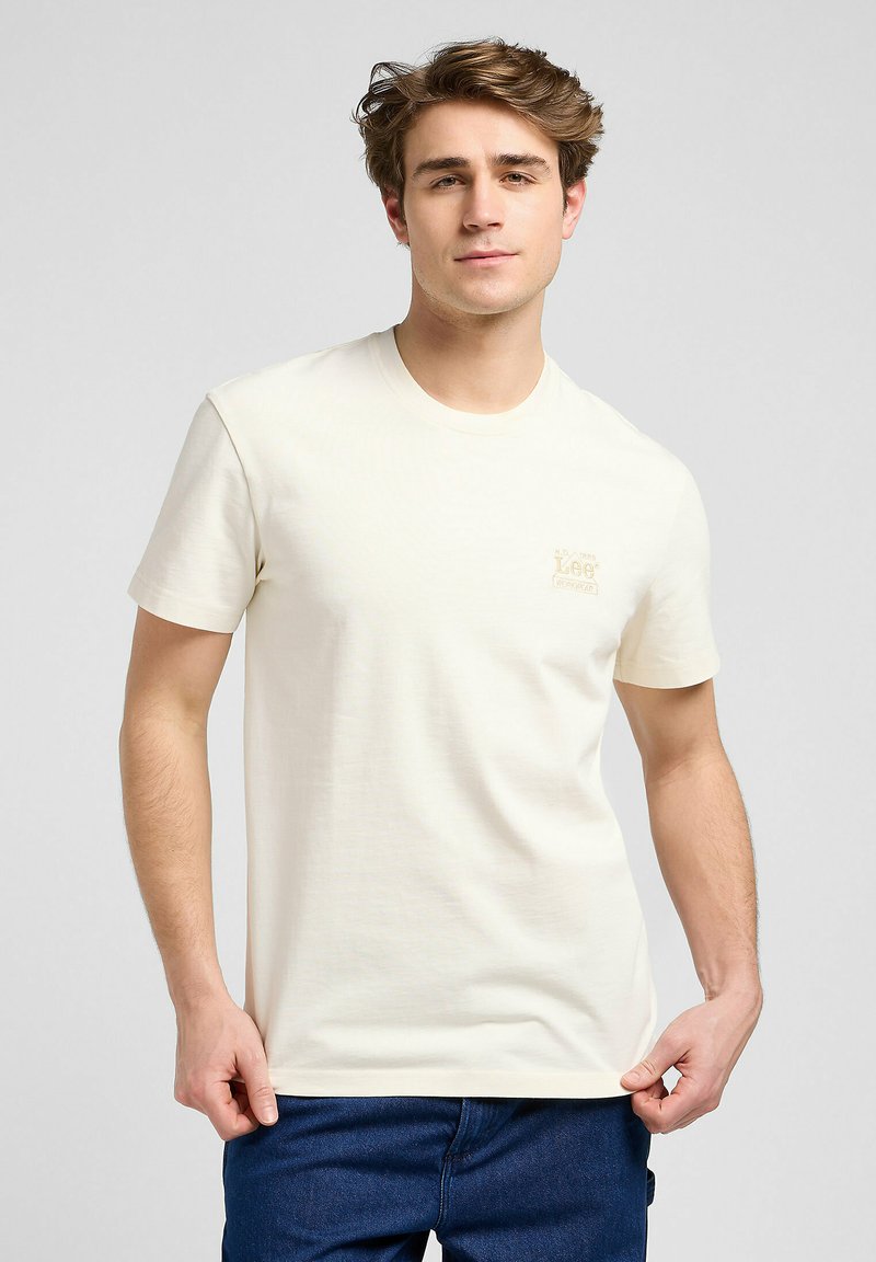 Creme kortærmet t-shirt lavet af blød bomuld. Den har et lille beige logo på venstre bryst og en klassisk rund halsudskæring.