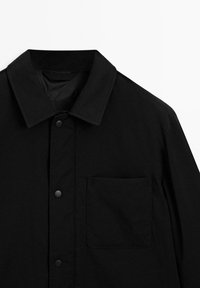 Black shirt featuring a classic collar, snap buttons, and a patch pocket, made of smooth fabric with a matte texture.