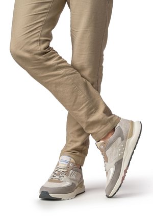 Sneakers in grigio chiaro e beige, con una tomaia testurizzata, dettagli in mesh e una suola bianca. La scarpa presenta lacci a contrasto e un marchio distintivo.