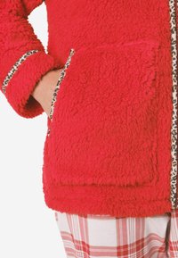 Czerwona kurtka z sztucznego futra z wstawkami w wzór panterki na kieszeniach i mankietach. Posiada kwadratowy fason oraz miękki, teksturowany materiał.