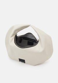 Beige kabelka vyrobená z hladkého koženkového materiálu, s kulatým tvarem, zipovým uzávěrem a černým interiérem se malou kapsičkou.