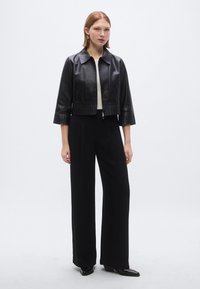 Μαύρο δερμάτινο κοντό μπουφάν με γιακά, με φερμουάρ και πλισέ τελείωμα. Συνδυάζεται με μαύρο παντελόνι με ψηλή μέση.