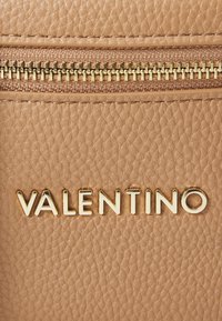 Šviesiai ruda odinė rankinė su lygiu paviršiumi, auksiniu užtrauktuku ir iškilmingu "VALENTINO" logotipu didžiosiomis raidėmis.