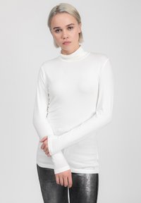 Maglietta bianca a maniche lunghe con collo alto, dal design aderente e dalla texture morbida, abbinata a leggings argentati metallici. Branding discreto sull'orlo.