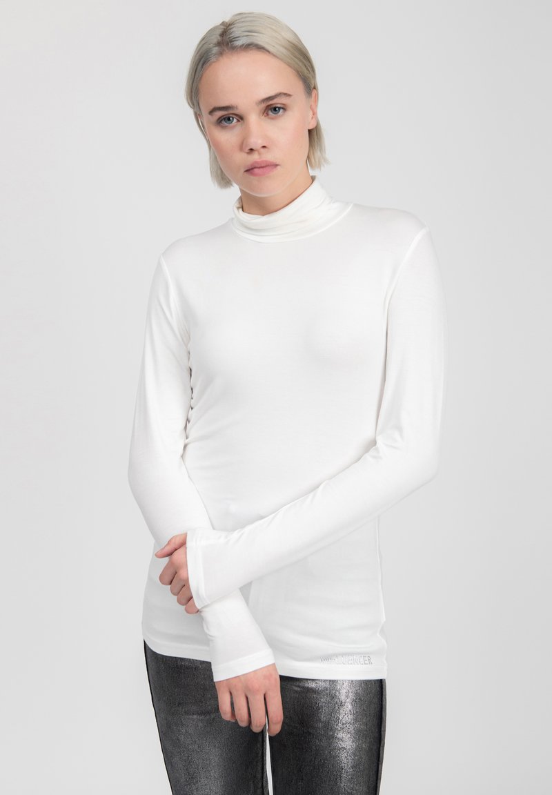 Maglietta bianca a maniche lunghe con collo alto, dal design aderente e dalla texture morbida, abbinata a leggings argentati metallici. Branding discreto sull'orlo.