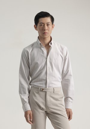 Camisa de vestir blanca con rayas verticales en azul claro, cuello abotonado y mangas largas. Pantalones beige con cierre de botón en la parte delantera.