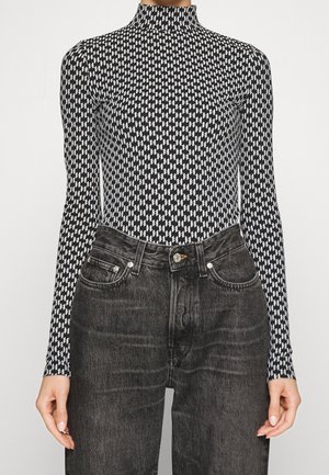 Body a maniche lunghe bianco e nero con colletto alto, caratterizzato da un motivo geometrico, abbinato a jeans scuri a vita alta.