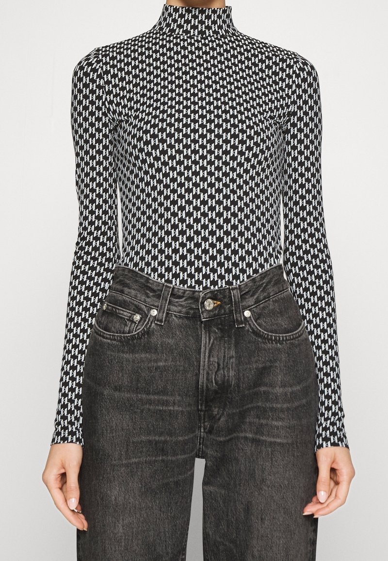 Body a maniche lunghe bianco e nero con colletto alto, caratterizzato da un motivo geometrico, abbinato a jeans scuri a vita alta.