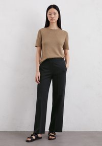 Brauner, gestrickter Kurzarmpullover kombiniert mit hoch taillierten, schwarzen, weit geschnittenen Hosen und schwarzen, flachen Sandalen mit minimalistischem Design.