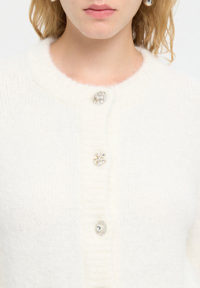 Weißer gestrickter Cardigan mit rundem Ausschnitt, drei dekorativen Kristallknöpfen und weicher Textur. Details umfassen gerippte Akzente.