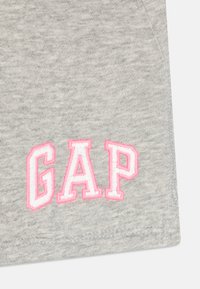 Pelēka kokvilnas auduma ar nedaudz teksturētu virsmu, kurā ir rozā izšūts "GAP" logos, rakstīts treknrakstā, blokveidā.