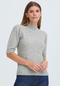 Světlé šedé svetrové tričko s krátkým rukávem a vysokým žebrovaným límcem. Měkká textura, přiléhavý střih a žebrovaný lem s ohrnutými okraji.