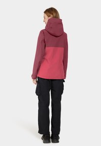 Veste imperméable de couleur rose foncé avec un panneau supérieur contrastant plus clair, dotée d'une capuche et de poignets réglables, assortie à un pantalon cargo noir.
