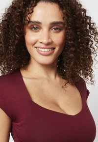 Haut ajusté bordeaux à manches courtes, avec un large décolleté incurvé et une texture lisse. Stylisé avec des détails froncés subtils.