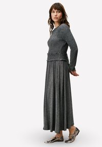 Haut gris à manches longues en maille avec une finition texturée et une taille smockée, associé à une jupe longue fluide grise. Chaussures plates argentées avec détail boucle.