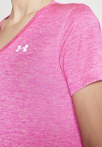 Roosa sportlik särk, millel on V-kaelus, lühikesed varrukad ja tekstuuritud muster. Rinna kohal on nähtav valge Under Armouri logo.
