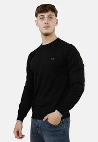 Maglione nero a maniche lunghe con scollo rotondo e dettagli grigi ai polsini. Presenta un piccolo logo nell'angolo superiore sinistro.