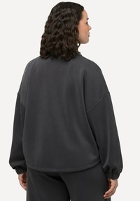 Szara, oversize bluza z gładką teksturą, z opadającymi ramionami i elastycznymi mankietami, prezentowana od tyłu. Pasujące doły nie są widoczne.