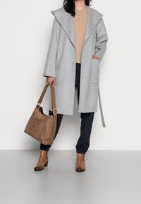 Cappotto di lana grigio con un grande cappuccio, due tasche frontali, abbinato a un maglione di lana color cammello, pantaloni scuri, stivali alla caviglia marroni e una borsa marrone scamosciata.